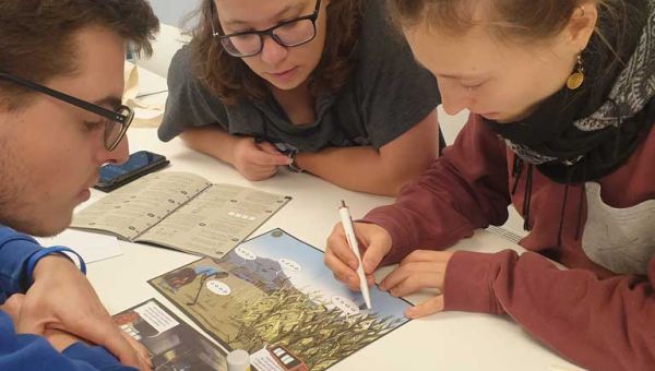 Drei Schüler sind über einen Tisch gebeugt und bearbeiten ein Arbeitsblatt.