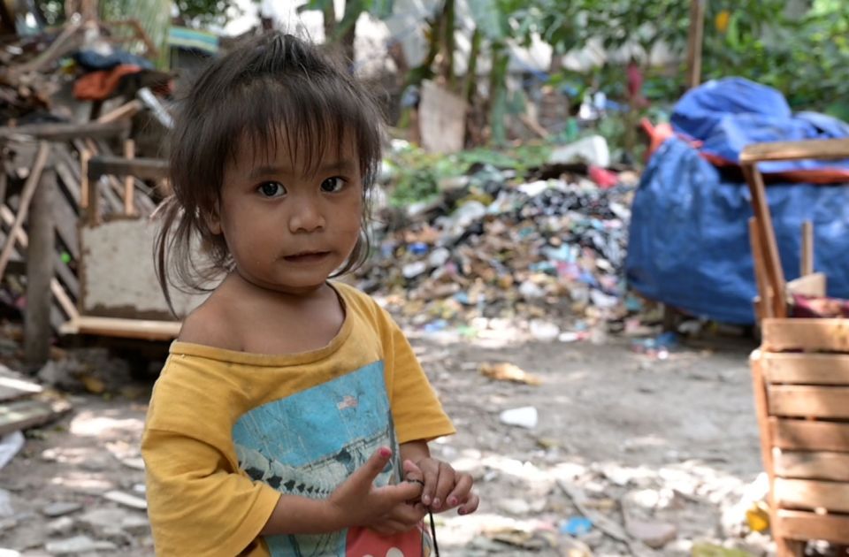 Josi, ein kleines Mädchen von den Philippinen in schmutziger Kleidung, steht in einer Gegend mit viel Müll