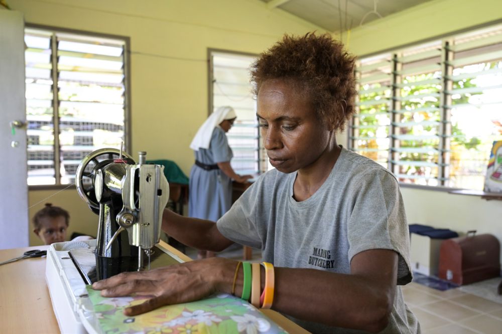 Eine Frau sitzt in Papua-Neuguinea in einem lichtdurchfluteten Raum an einer Nähmaschine und näht konzentriert.