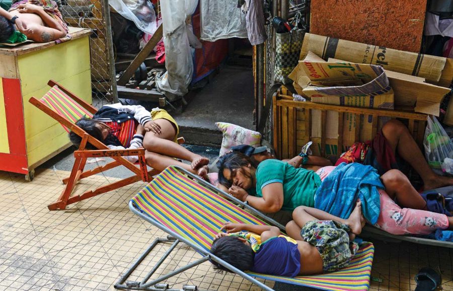 Eine Frau schläft mit ihren Kindern am Rand einer Straße in Manila auf einem Bretterverschlag. Zwei Kinder schlafen auf Klappstühlen.